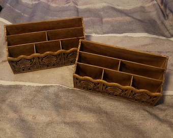 May include: Two wooden desk organizers with multiple compartments. The organizers are a warm brown color and feature carved floral designs along the bottom edge. The organizers are designed to hold letters, documents, or other office supplies.