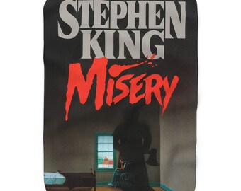 May include: A black blanket featuring the cover art of Stephen King's novel "Misery." The title is in bold red letters with a blood splatter effect. The image depicts a shadowy figure with an axe, a person in a wheelchair, and a bed.