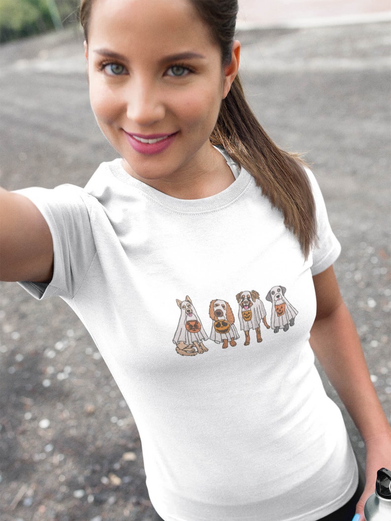 Puede incluir: Camiseta blanca con un gr&aacute;fico de cuatro perros disfrazados de fantasmas para Halloween. Los perros llevan s&aacute;banas blancas con agujeros para los ojos y llevan cubos de calabaza.