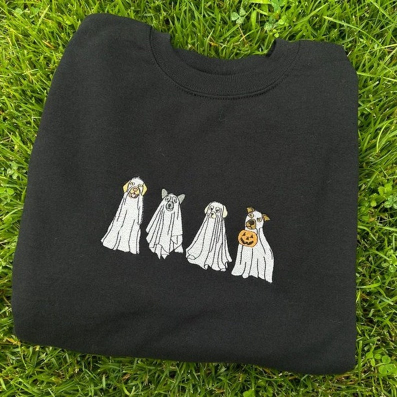 以下が含まれることがあります： ハロウィンのために幽霊に扮した4匹の犬の刺繍が施された黒いスウェットシャツ。1匹の犬がカボチャを持っています。