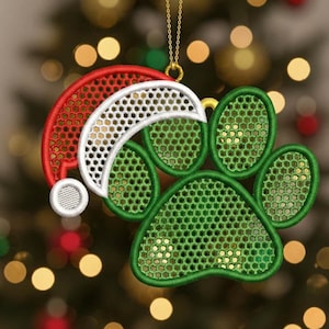 May include: Embroidered Christmas ornament featuring a green paw print and a Santa hat in red and white. The ornament is suspended by a gold chain, perfect for pet lovers during the holiday season.