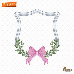 以下が含まれることがあります： 白い縁取りとピンクのリボンが下部にある、盾型のフレームが特徴の刺繍デザイン。リボンの両側には緑の葉があります。「5 Sizes」の文字が左上にあります。