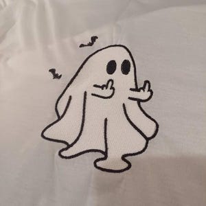 May include: White fabric with a black embroidered ghost design. The ghost has two black eyes and is giving the middle finger with both hands. Two small black birds are above the ghost.