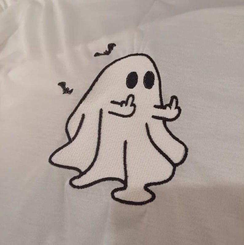 May include: White fabric with a black embroidered ghost design. The ghost has two black eyes and is giving the middle finger with both hands. Two small black birds are above the ghost.