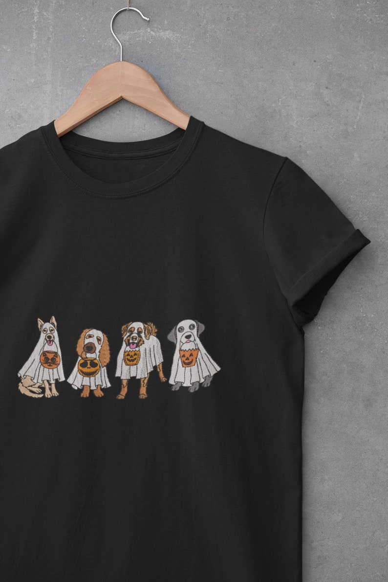 Puede incluir: Camiseta negra con un gr&aacute;fico de cuatro perros disfrazados de fantasmas que llevan bolsas de truco o trato. Los perros llevan disfraces de fantasmas blancos con cubos de calabaza naranja y negro.