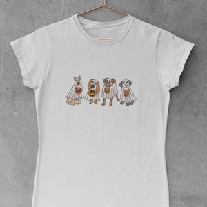 Puede incluir: Una camiseta blanca con un gr&aacute;fico de cuatro perros disfrazados de fantasmas que sostienen calabazas. Los perros son un perro blanco, un perro marr&oacute;n y blanco, un perro marr&oacute;n y un perro gris.