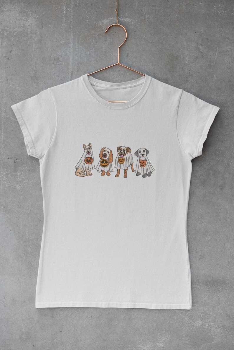 Puede incluir: Una camiseta blanca con un gr&aacute;fico de cuatro perros disfrazados de fantasmas que sostienen calabazas. Los perros son un perro blanco, un perro marr&oacute;n y blanco, un perro marr&oacute;n y un perro gris.