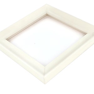 May include: A white picture frame with a simple, slightly raised edge. The frame is made of wood and has a smooth finish.