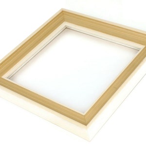 May include: A rectangular picture frame with a layered design. The frame has a light wood-colored inner border and a white outer border. The frame is empty, with a clear opening in the center.