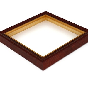May include: A square picture frame with a dark red wood exterior and a gold interior. The frame is empty.