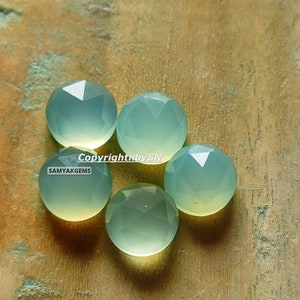 May include: Five faceted, light green chalcedony gemstones on a wooden surface. Copyright by SN SAMYAKGEMS.