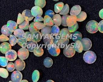 May include: A collection of round, iridescent opal gemstones in various shades of white, with flashes of rainbow colors. The gemstones are scattered on a black surface.
