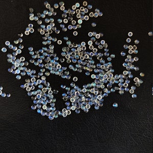 May include: A large group of iridescent blue and white round gemstones on a black surface.