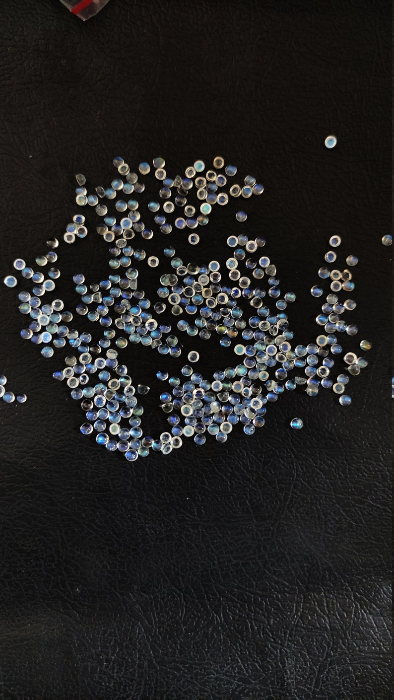 May include: A large group of iridescent blue and white round gemstones on a black surface.