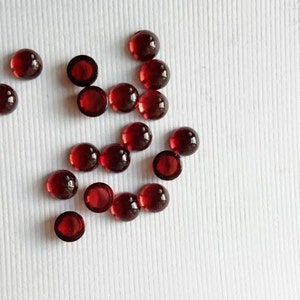以下が含まれることがあります： 白い表面に散らばった、丸い赤い宝石のカボションの集まりです。