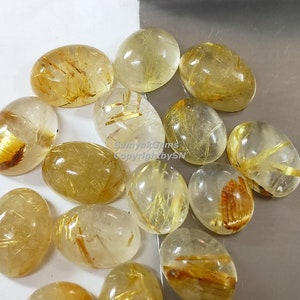 以下が含まれることがあります： 透明な金色のルチルクォーツの楕円形のカボションの集まり。石はクリアでガラスのような外観で、キラキラ光る糸のような金色のインクルージョンがあります。