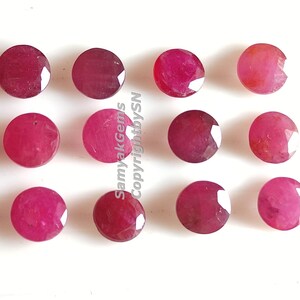 May include: Twelve round, faceted, red gemstones. The gemstones are arranged in four rows of three. The gemstones are on a white background.