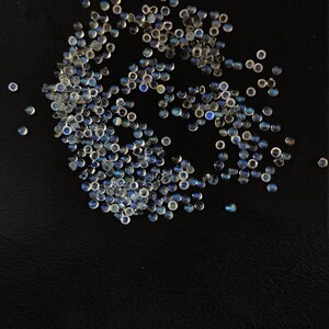 May include: A large group of iridescent blue and white gemstone cabochons, scattered on a black surface.