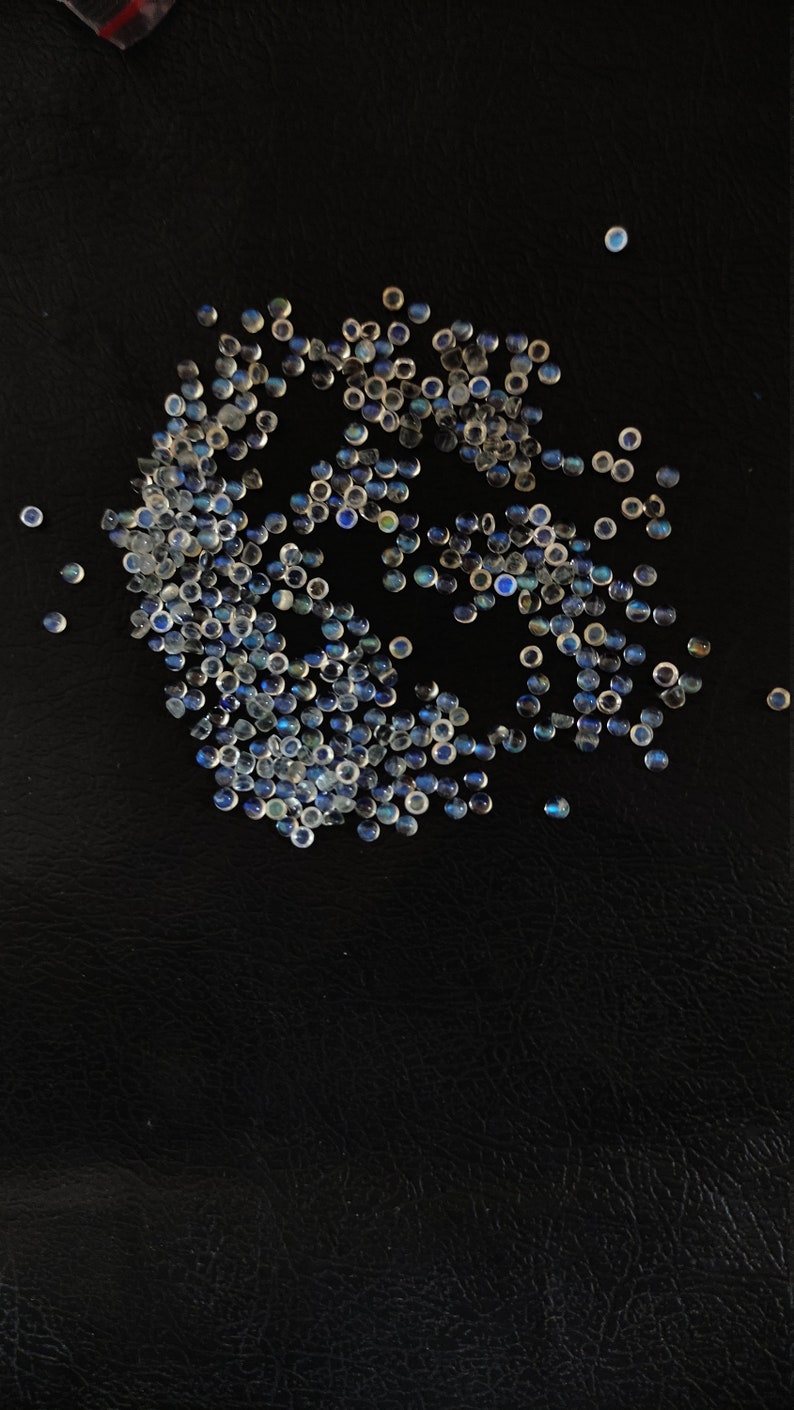 May include: A large group of iridescent blue and white gemstone cabochons, scattered on a black surface.