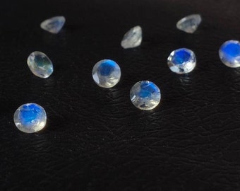 May include: A collection of eight iridescent moonstone gemstones, each with a round, faceted shape. The stones are arranged in a scattered pattern on a black surface.