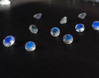 May include: A collection of round, iridescent moonstone gemstones with a blue sheen, scattered on a black surface.