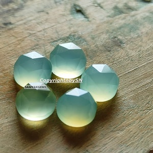 May include: Five faceted, light green gemstone beads on a wooden surface. The beads are round and have a smooth, polished finish. Copyright by SN SAMYAKGEMS