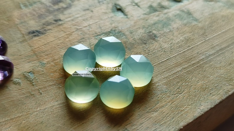 May include: Five faceted, light green gemstone beads on a wooden surface. The beads are round and have a smooth, polished finish. Copyright by SN SAMYAKGEMS