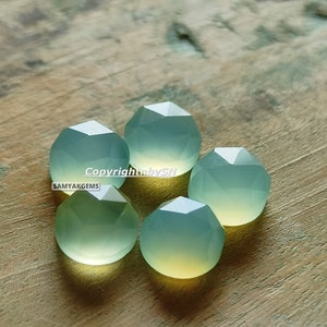 May include: Five faceted green chalcedony gemstones on a wooden surface. The gemstones are a light green colour with a slight yellow hue. The text "Copyright by SN SAMYAKGEMS" is visible in the image.