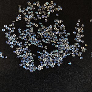 May include: A scattering of iridescent blue and white gemstone cabochons on a black surface.