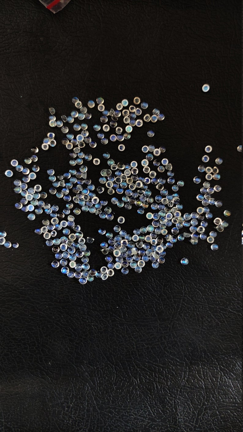 May include: A scattering of iridescent blue and white gemstone cabochons on a black surface.
