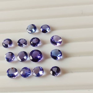 May include: A collection of round, purple gemstones, likely amethyst or topaz, arranged on a white surface.
