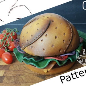 Op de afbeelding: Een leren hamburger met een bruin broodje, sla, tomaat en ui. De hamburger ligt op een houten snijplank met tomaten op de achtergrond. De afbeelding bevat de tekst "Pattern" en een logo voor Beardfoot.