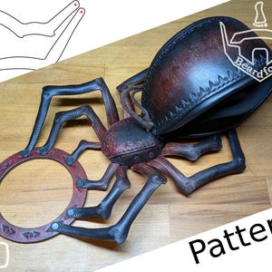 Puede incluir: Accesorio de cuero artesanal con forma de araña, en tonos marrón oscuro y rojo. El diseño incluye un marco circular, múltiples patas y un cuerpo central. La palabra "Pattern" es visible en la imagen.