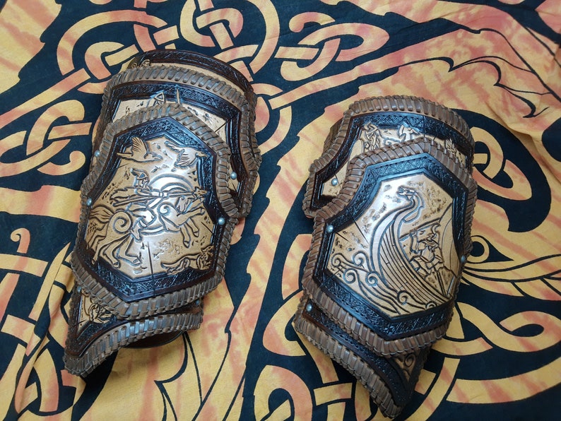 May include: A pair of brown leather arm guards with intricate carvings. One guard features a Viking ship with a dragon head, while the other depicts a mythical creature with wings.
