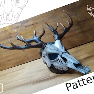 May include: A white deer skull mask with antlers, painted in brown and white. The mask has a leather strap and is on a wooden surface. The text "Pattern" is visible in the bottom right corner of the image.
