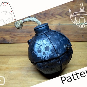 Puede incluir: Un objeto esférico de cuero negro con forma de bomba de dibujos animados con una mecha de cuerda de yute gruesa en la parte superior. La superficie presenta un emblema de calavera estampado y un patrón de engranajes, fijado con remaches.