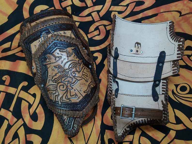 May include: Two leather arm guards, one brown with a detailed design and the other white with black straps. Both have decorative stitching.