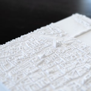 May include: A white 3D printed model of a city skyline. The model is detailed and shows the buildings and streets of the city.