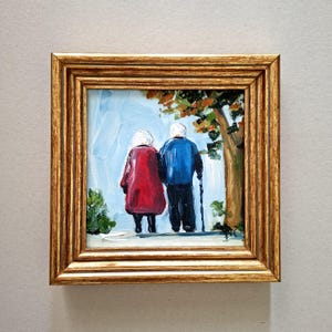 以下が含まれることがあります： 金色の額縁に入った油絵で、後ろ姿の二人の人物が描かれています。一人は赤いコートを着ており、もう一人は青いジャケットを着て黒い杖を持っています。彼らは、水色の空を背景に、緑とオレンジの葉を持つ木のそばに立っています。