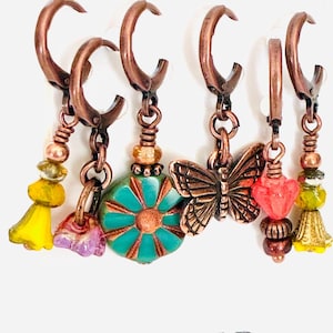 May include: A set of six copper-toned leverback stitch markers featuring various charms including a turquoise flower, a butterfly, and yellow and pink glass beads. The text BAYOU-BIRD co. is printed at the bottom of the display card.