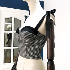 May include: A black and white checkered crop top with black straps and bows on the shoulders.
