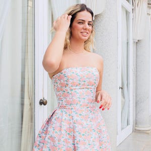 Nuestra modelo lleva un hermoso vestido color coral, elegante, con un encantador estampado floral y espalda al aire, ideal para tus invitaciones a una boda, fiesta de graduación o cóctel."