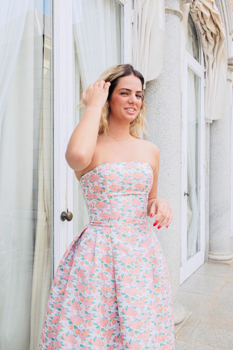 Nuestra modelo lleva un hermoso vestido color coral, elegante, con un encantador estampado floral y espalda al aire, ideal para tus invitaciones a una boda, fiesta de graduación o cóctel."