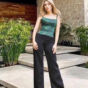 May include: A woman wearing a green and blue patterned tank top with black straps and black wide-leg pants. The outfit is worn outdoors in front of a building with a stone facade and concrete steps.