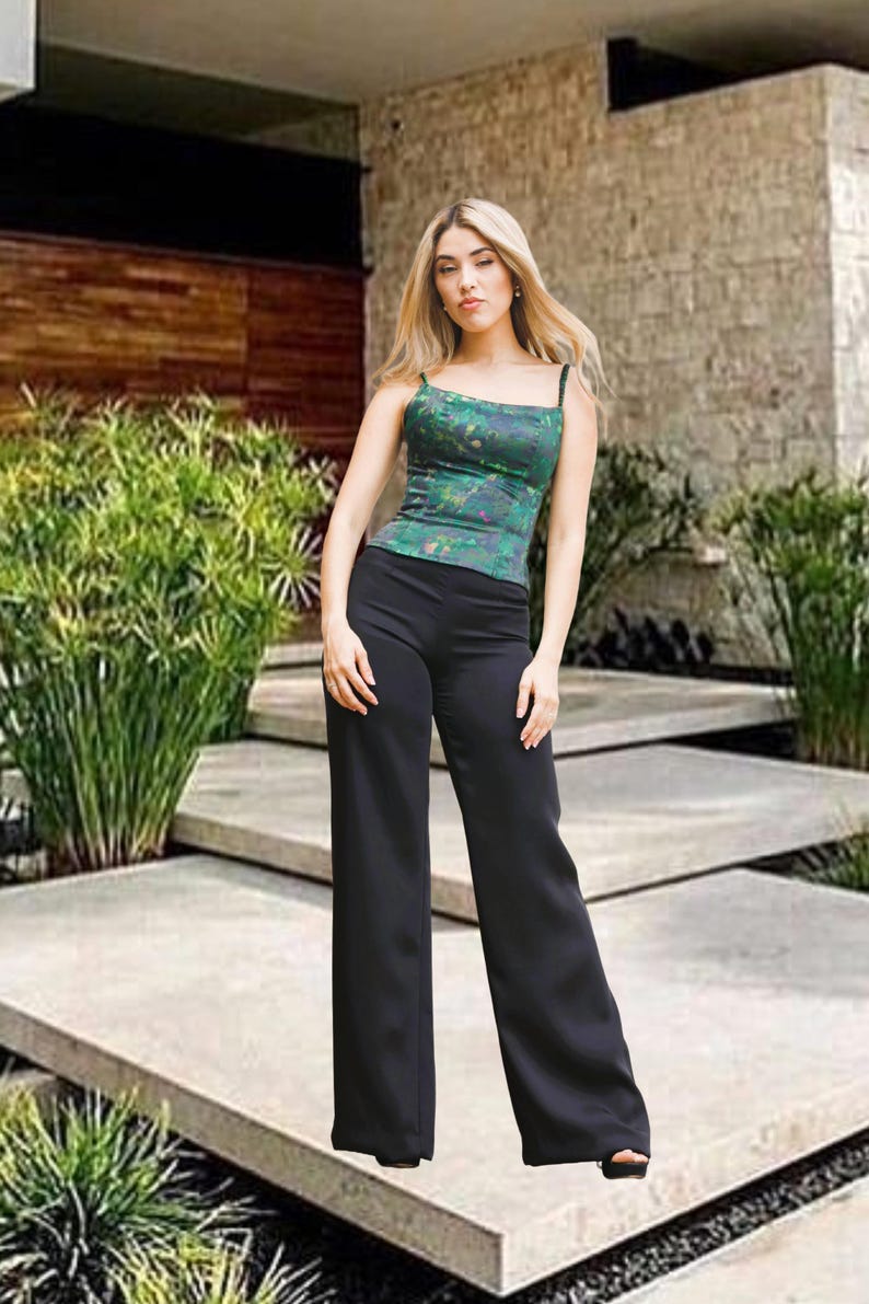 May include: A woman wearing a green and blue patterned tank top with black straps and black wide-leg pants. The outfit is worn outdoors in front of a building with a stone facade and concrete steps.