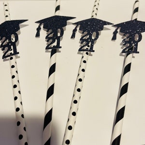 Puede incluir: Cuatro pajitas rayadas en blanco y negro con gorros de graduaci&oacute;n de purpurina negra unidos. Los gorros tienen el a&ntilde;o 2021 impreso en ellos.