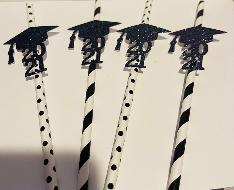 Puede incluir: Cuatro pajitas rayadas en blanco y negro con gorros de graduaci&oacute;n de purpurina negra unidos. Los gorros tienen el a&ntilde;o 2021 impreso en ellos.