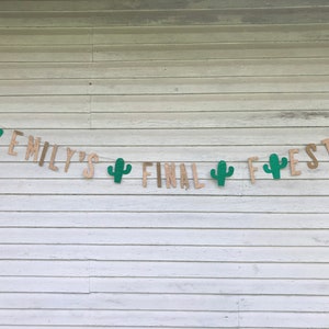 Puede incluir: Una pancarta de arpillera con el texto "Emily's Final Fiesta" en letras doradas con purpurina. Se han enhebrado recortes de cactus verdes entre las letras.