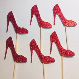 May include: Six red glitter high heel shoe cupcake toppers on wooden sticks.