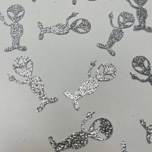 May include: Silver glitter alien confetti. The aliens are in a variety of poses, including waving and pointing.